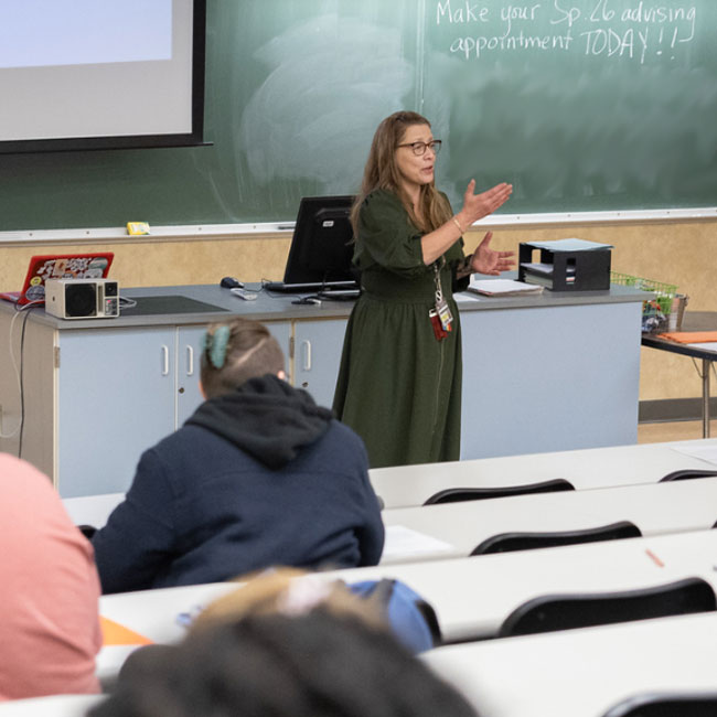 A female teacher stands in front of a chalkboard and speaks to a class in a lecture hall at Columbia Greene Community College