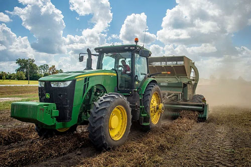 A large green tractor plows a farm field.