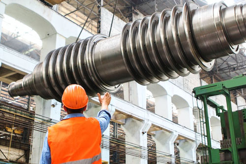 A man in an orange safety vest looks up at large pipe in advanced manufacturing warehouse.
