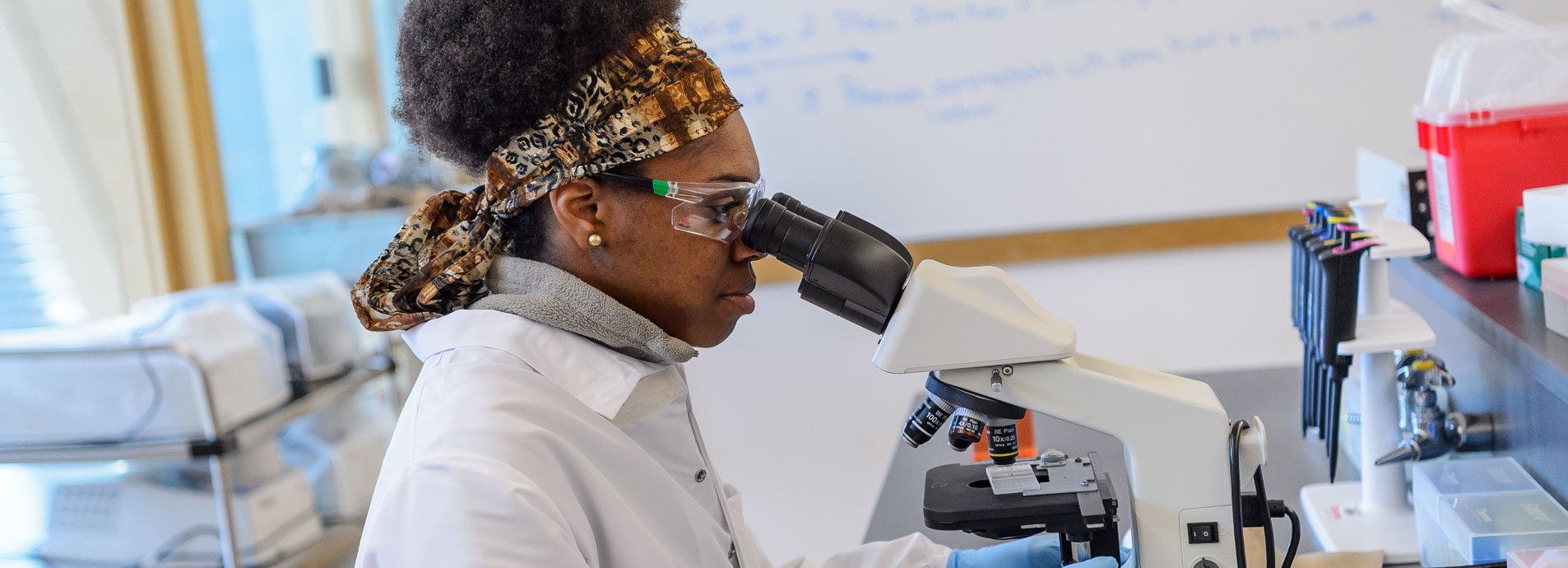 An african american female student looks into a microscope