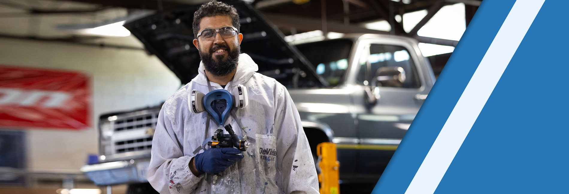 Male in an auto repair garage wearing vinyl cover suit for painting.