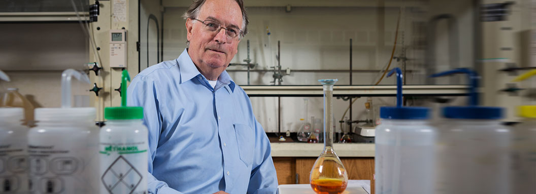 Binghamton University professor Stanley Whittingham stands behind a table in a science lab.