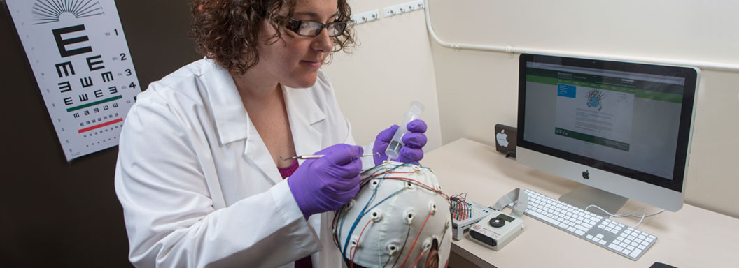 Female researcher at Binghamton University looks looks at subject's head.
