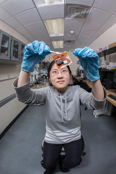 A female researcher at Binghamton University looks up at a computer chip. 