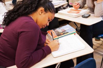 Female african-american college student writes at desk in school.