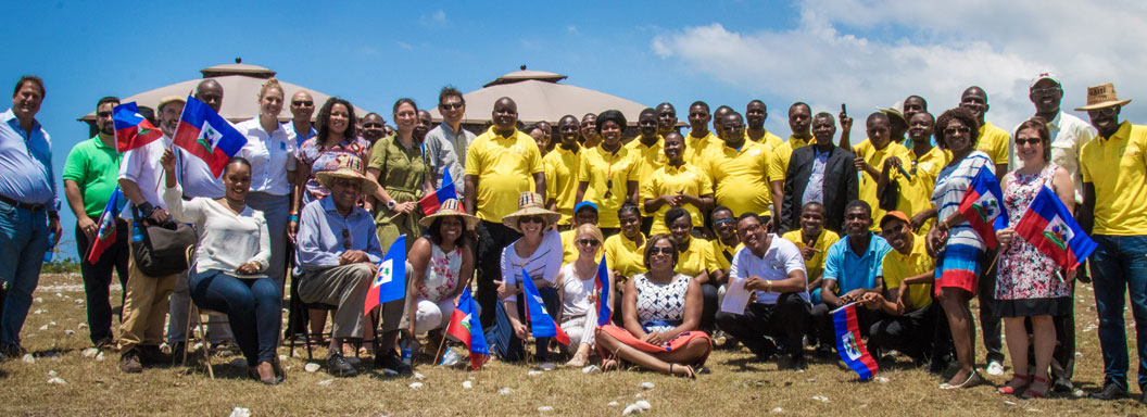 SUNY officials and locals dressed in yellow from Akaye, Haiti pose for large group photo outside on land that will be the SVLC.