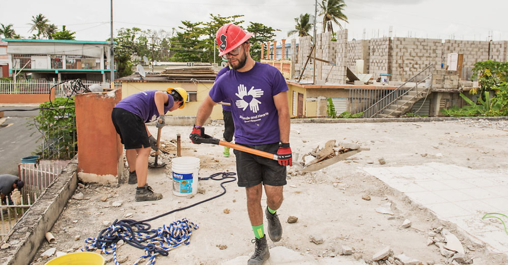 A College at Brockport student carries debris in a shovel on a rooftop in Puerto Rico.