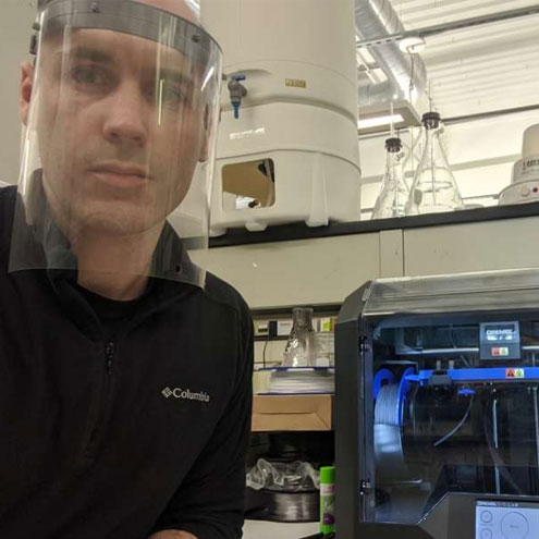 SUNY Polytechnic Institute staffer wears a PPE mask printed in a school facility.