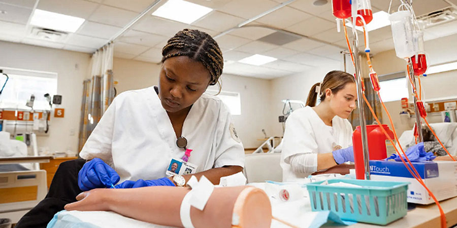 Two female medical students work in a hospital simulation room.