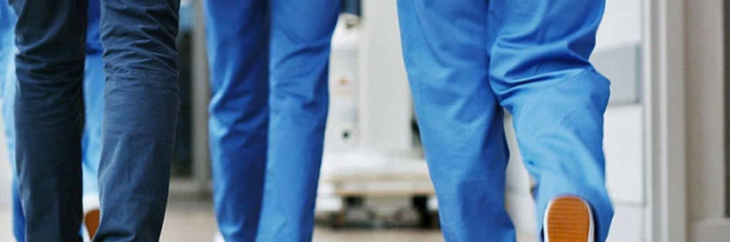 View of the backs of legs of various medical staff walking down a hall in hospital.