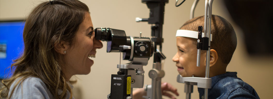 An eye doctor looks through a machine into child's eyes.