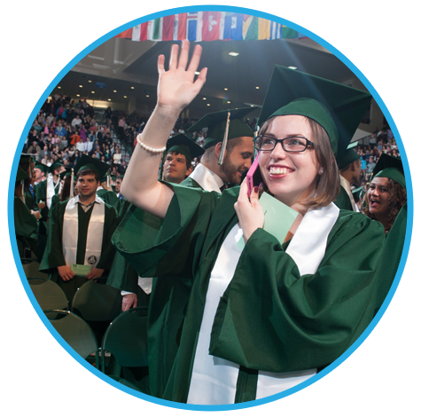 Female graduate smiles and waves while on cell phone during Binghamton University graduation ceremony.