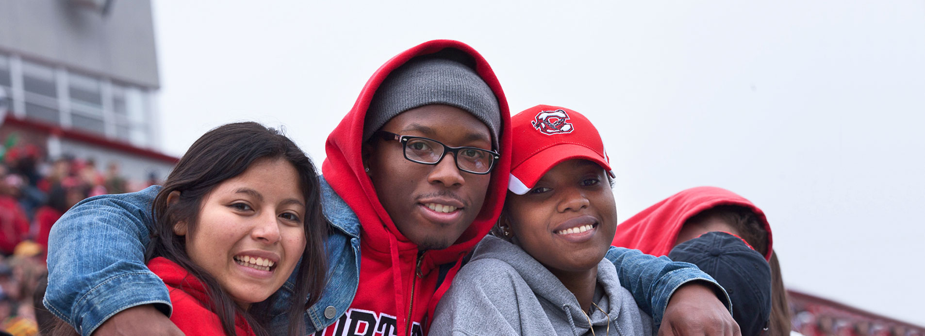 SUNY Cortland students smile for the camera in the stands at a football game.