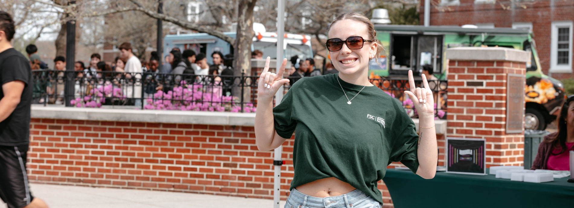 A female student at Farmingdale State College gives holds her hands up while giving the hook em horns sign on them at a campus outdoor event.