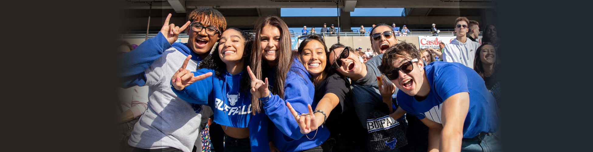 University at Buffalo fans cheer hard while leaning on a railing in the stands at the UB Bulls football game.