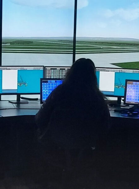 A person sits at their station in an airport tower while working air traffic control systems.