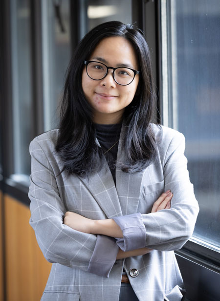 Asian american female college student stands with her arms crossed in a glass walled hallway.