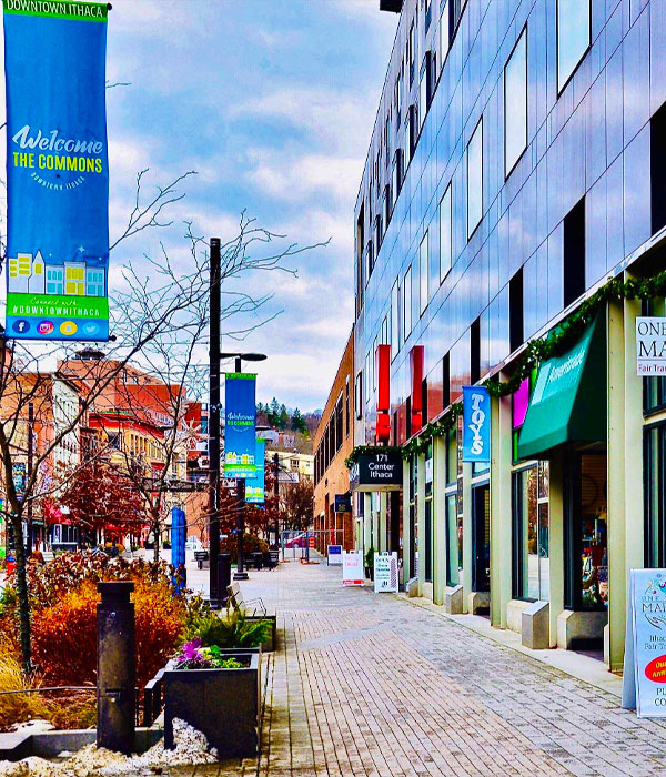 Downtown Ithaca Commons sidewalk along a row of shops and cafes with banner on street pole saying Downtown Ithaca - Welcome, the Commons