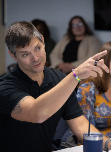 A man in black polo shirt points at something he's referencing off screen.