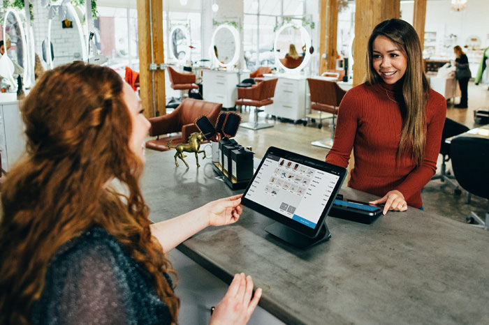 Female talks to female staff at a beauty salon front desk.