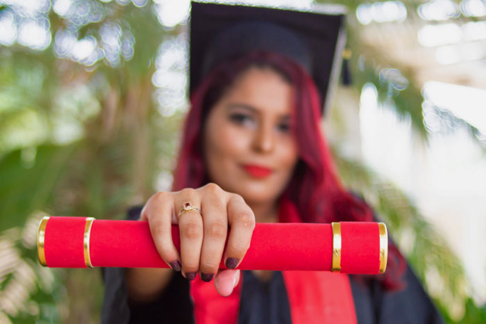 Female college graduate holds a rolled up diploma in her hand.
