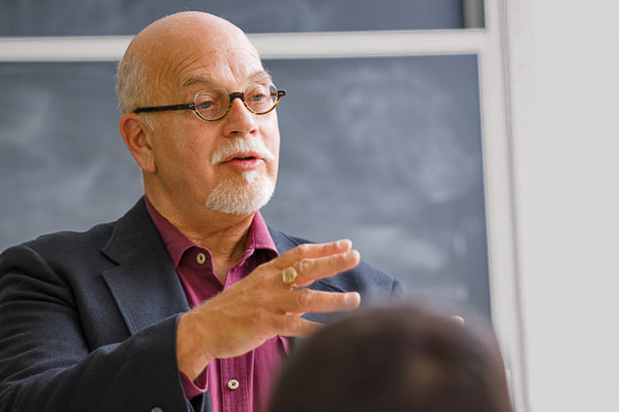 Older male professor speaks to class.