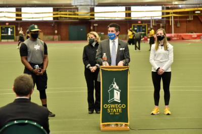 Chancellor Malatras speaks at a podium at the SUNY Oswego field house during a press event about spring 2021 sports competition.	
