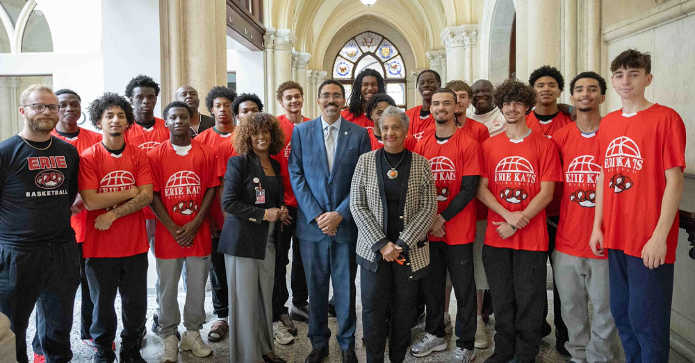 SUNY Chancellor John B. King Jr. stands with SUNY Trustee Eunice Lewin and a group of the 2026 EOP Scholars from Erie Community College wearing orange Erie Kats tshirts.