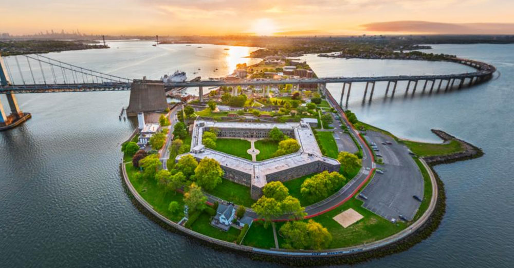 Aerial view of SUNY Maritime College campus with the Throggs Neck Bridge showing over the top of it and the NYC East River all around it.