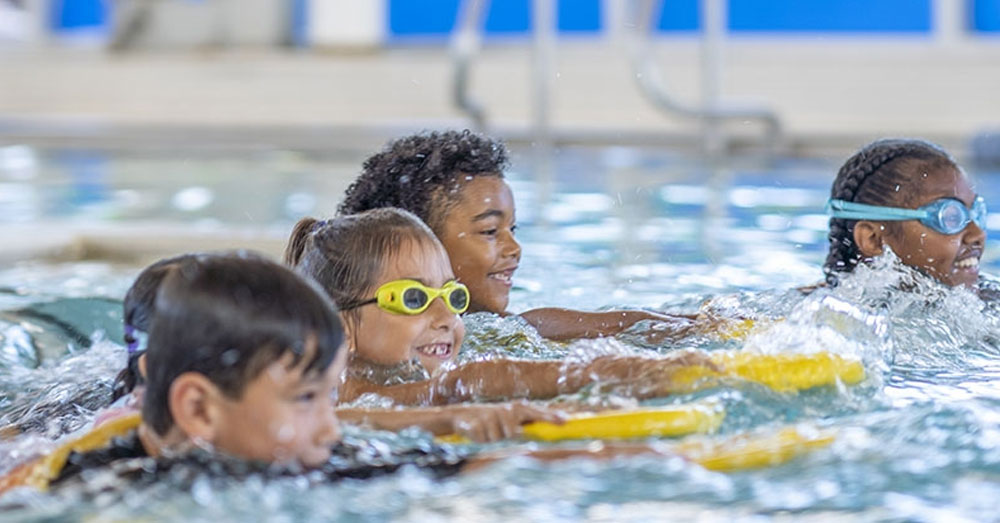 Young children swim together in a large inground swimming pool. 