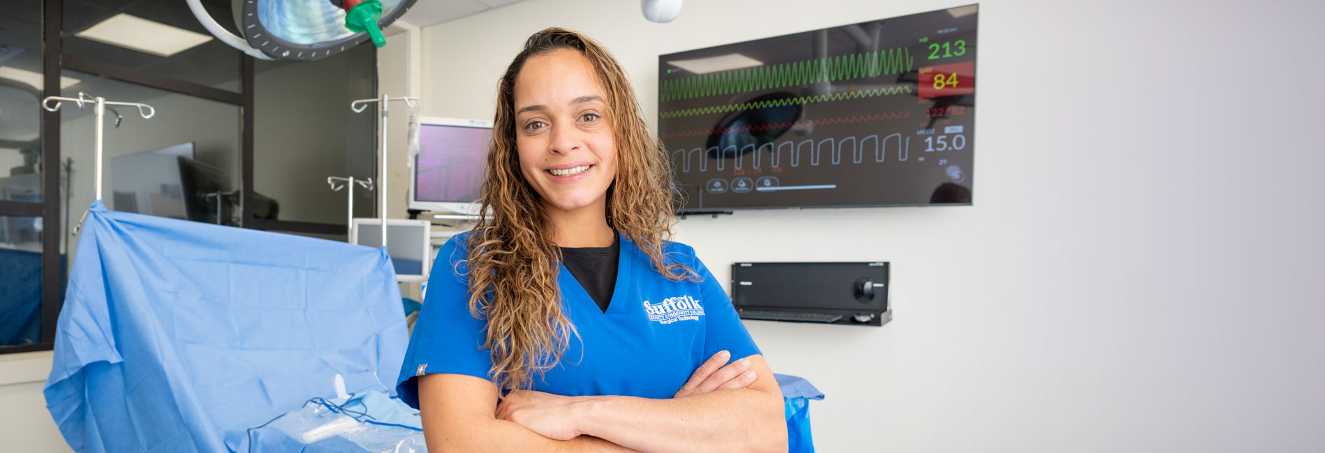 Nursing student in blue scrubs with SUNY Suffolk logo on the chest.