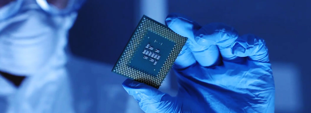 A researcher holds a computer chip in blue light.