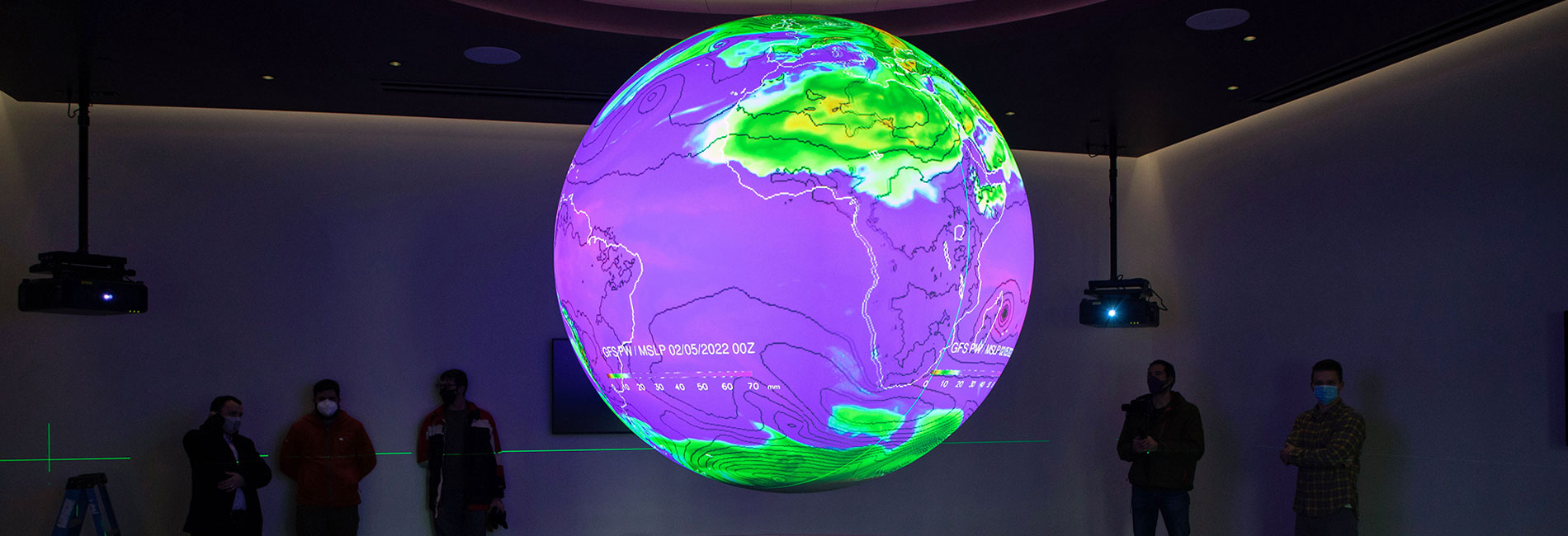 A bright hologram of a globe shines in a dark room with people looking at it.