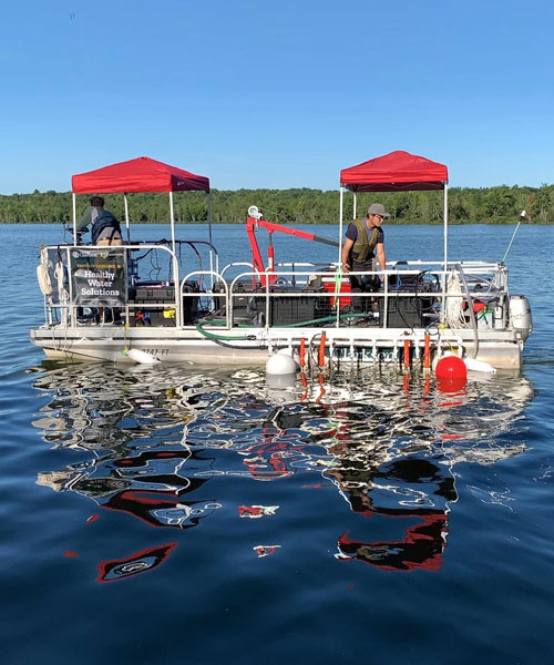 A pontoon boat sits idle in a lake with research equipment on it for water testing.