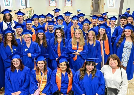 Many students dressed in blue graduation caps and gowns pose for a picture.