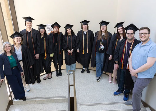 SUNY Fredonia ACE students ready for graduation dressed in black caps and gowns.