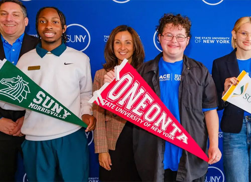 SUNY students stand with pennants in hand in front of blue SUNY brand backdrop.