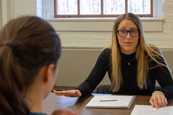 A female academic advisor speaks to a college student in her office.