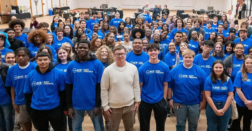 Large number of ACE students with blue tshirts on gather for a group photo in a SUNY Oneonta gym.